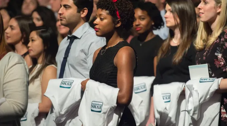 A crowd of EVMS students hold white coats during a ceremony