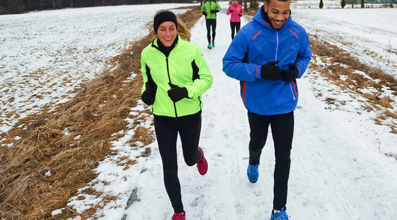 Four people dressed in bright winter clothing jog on a snow-