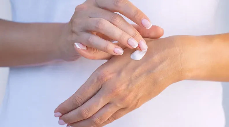 Close-up of a woman's hands. She is applying moisturizer to 