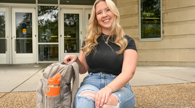 A woman sits on some steps in front of a building on ODU's campus. 