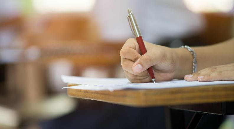 Closeup to hand of student holding pen and taking exam in cl
