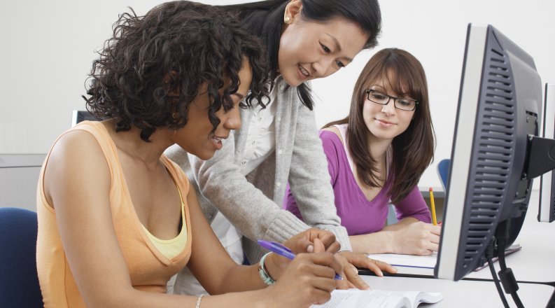 Two female students working with teacher in computer classro