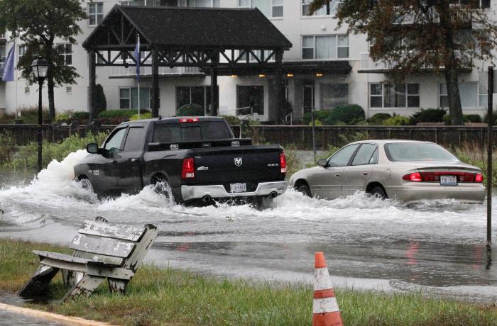 a black pick-up truck and a white sedan drive through a flooded street