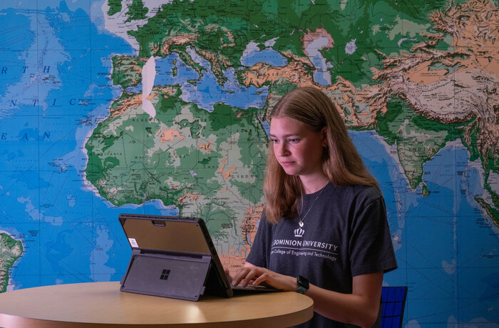 Student on a laptop with a world map behind them