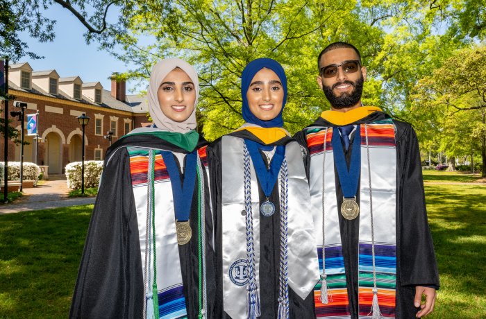 Sana, Seena and Fozi Alkaifi pose in graduation regalia with Rollins Hall in the background.