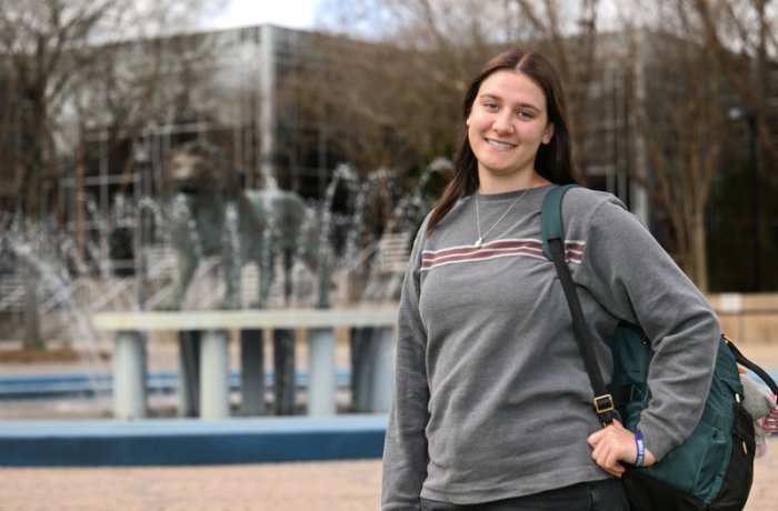 Amie Burdette stands in front of the Old Dominion University lion fountain, holding a backpack and smiling.