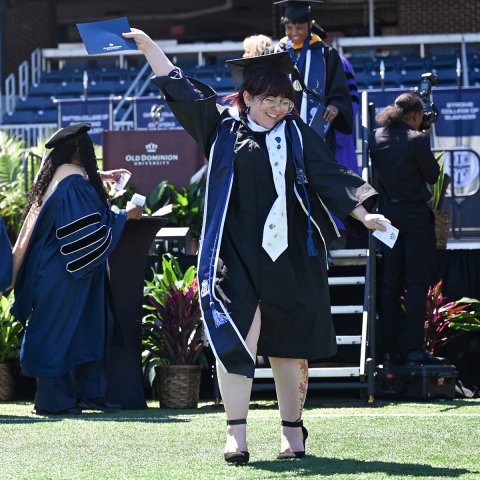 Graduate celebrating walking off the Commencement stage in SB Ballard stadium.