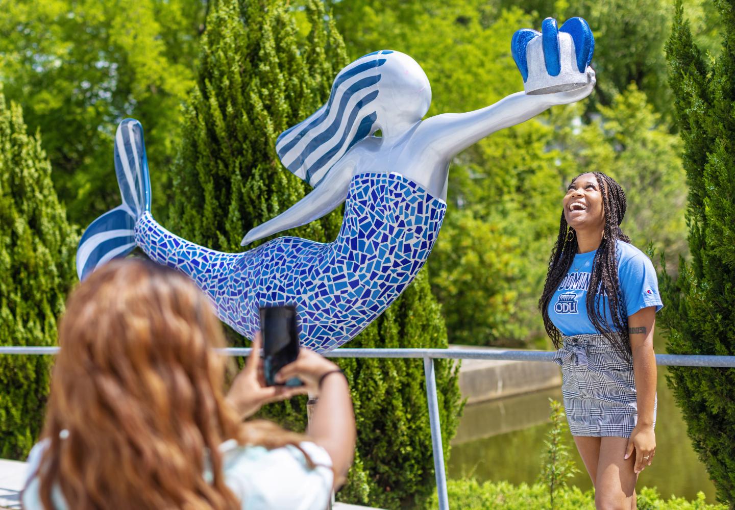 A female ODU students stands underneath reign the mermaid stature