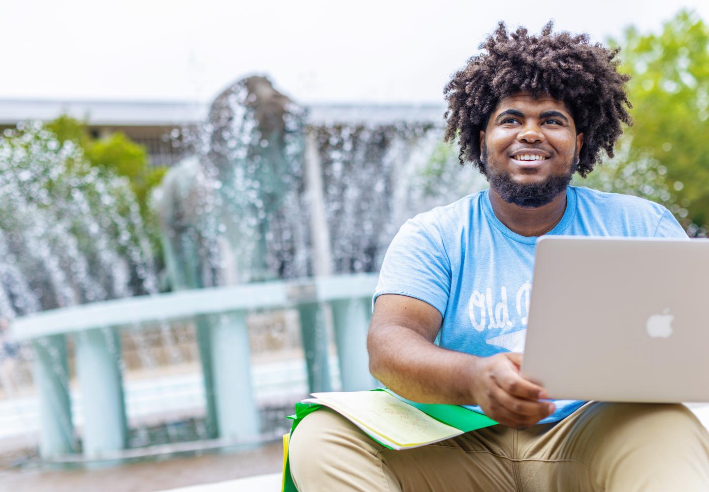 an ODU student is sitting in front of the lion fountain with a laptop