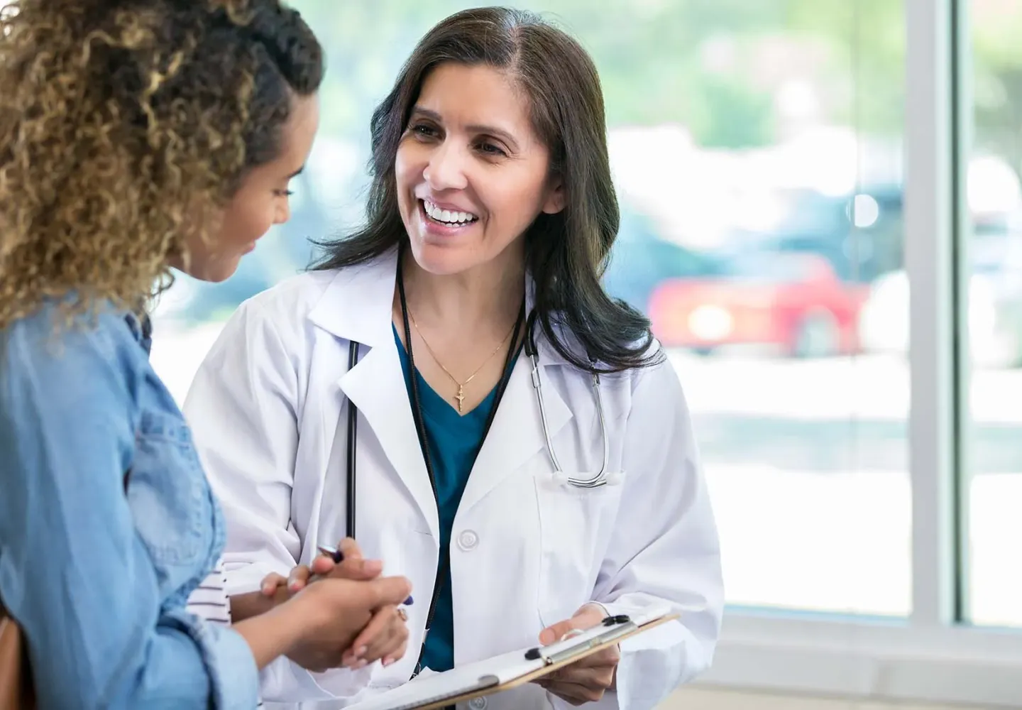 A female doctor holding a clipboard speaks to a patient.