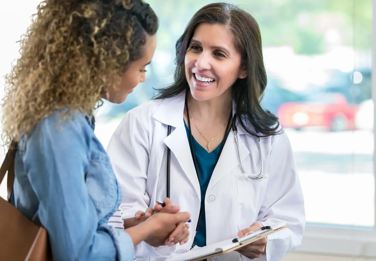 A female doctor holding a clipboard speaks to a patient.