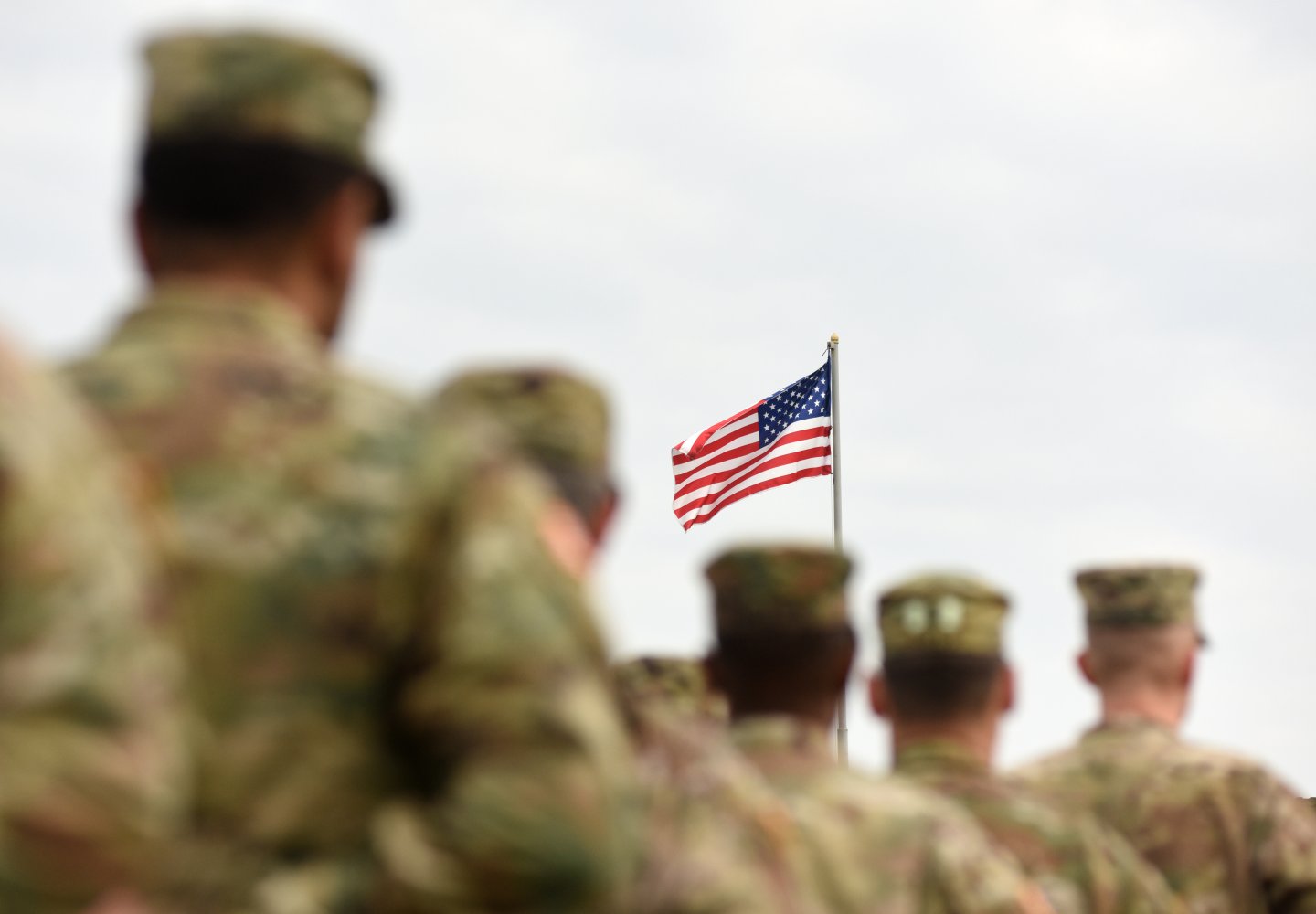 American soldiers in formation look at American flag on top of pole waving in the wind.