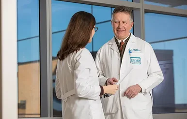 An older male physician speaks with a female resident
