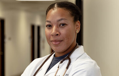 Nursing student in white coat smiles while holding clipboard.