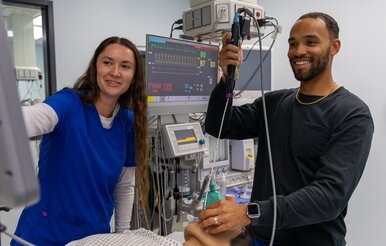 Two nursing students practice performing procedure on mannequin.