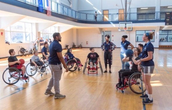 Students working with kids in wheelchairs in ODU gym