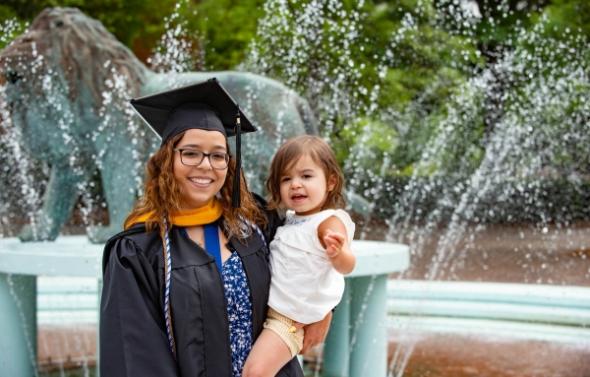 woman in graduation garb with her child in front of the lion fountain
