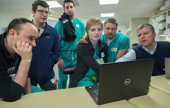 Students and faculty gather around a computer during a lesso