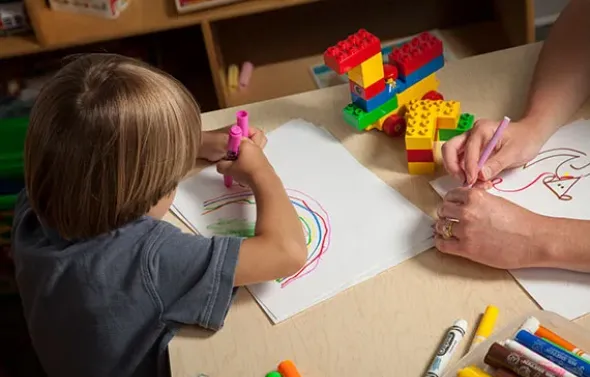 A fellow observes a child drawing.