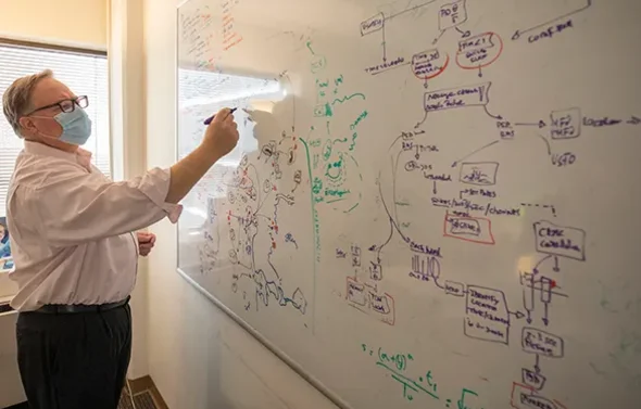 A male writes on a dry erase board already covered in severa