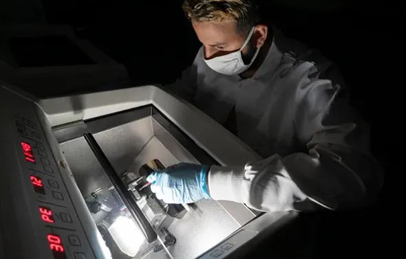 Male in gloves and mask working at a large piece of lab equi