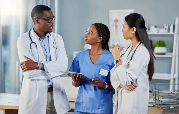 Three doctors and a woman in blue scrubs discuss a report
