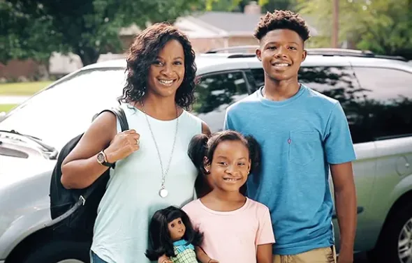 A family poses in front of a vehicle.