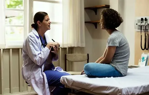 A physician talks with a patient in an exam room.