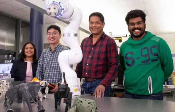 Group of engineering students standing next to robotic arm