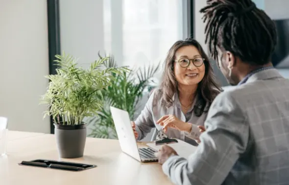 Two people chatting in the office in front of a laptop