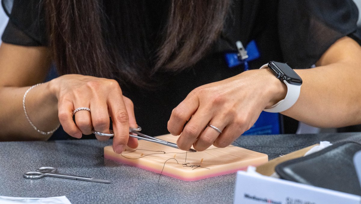 Closeup of female nursing student hands cutting suture thread with scissors.