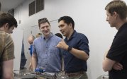 Four young men discuss model structure on table in front of them