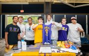 A group of students stand behind a table. 