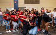 A group of students stand together and make their sorority sign with their hands. 