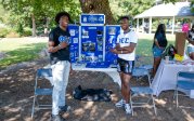 Two students stand in front of a table. 