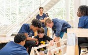 Four students build a project using wood, while two others look on.