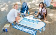 Students paint a crown on a sidewalk. 