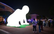 A group of people stand around an illuminated large-scale sculpture of a human figure.