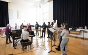A woman leads students in a vocal exercise in a music room.