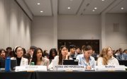 A group of students sit at tables in a conference room.