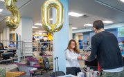 woman hands cake to a man in front of baloons