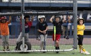 Young baseball players stand behind a screen and await their turn at bat.