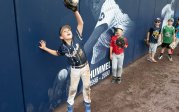 A young baseball player makes a catch at the outfield wall.