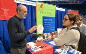 A man talks to a woman at an information table. 