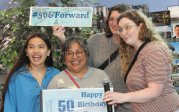 four people pose with signs in library