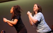  Two young women wearing Monarchs Move t-shirts lean forward for part of their dance recital.