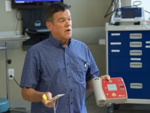 A man holding a heart device and talking to students