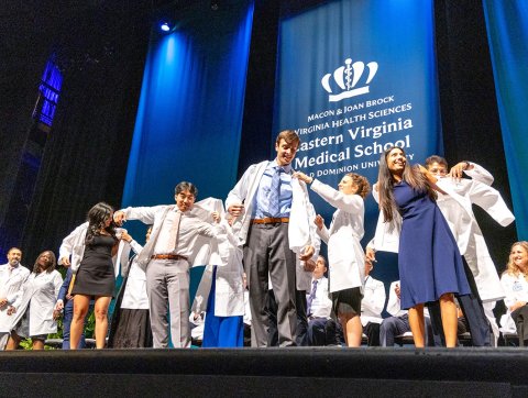 MD students on stage receiving white coats. 