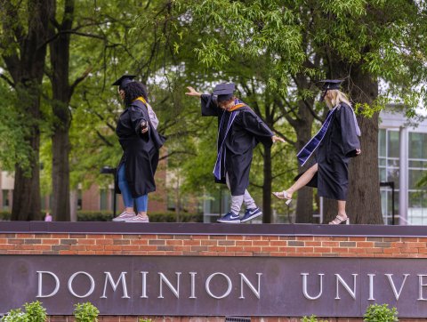 three odu students walk across the ODU sign in caps and gowns