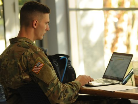 A student in military uniform works on their laptop. 
